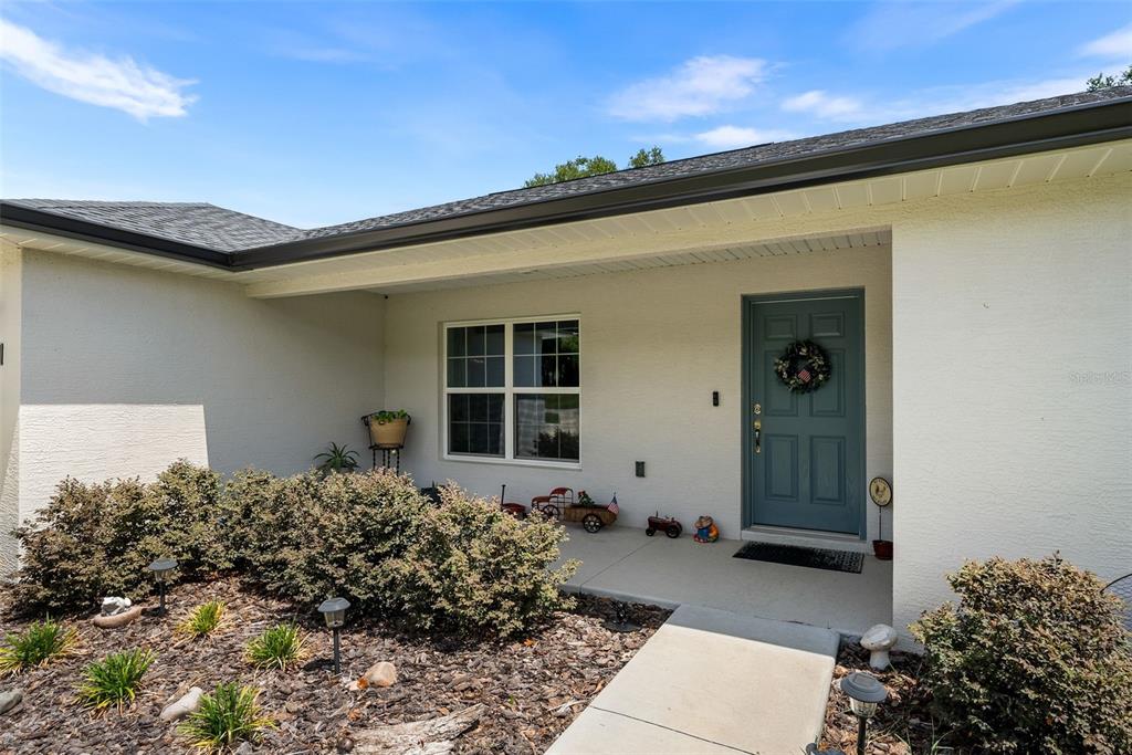 A light-colored house exterior features a blue front door, a concrete walkway, and landscaping — 1831 NE 160TH PLACE, CITRA, FL