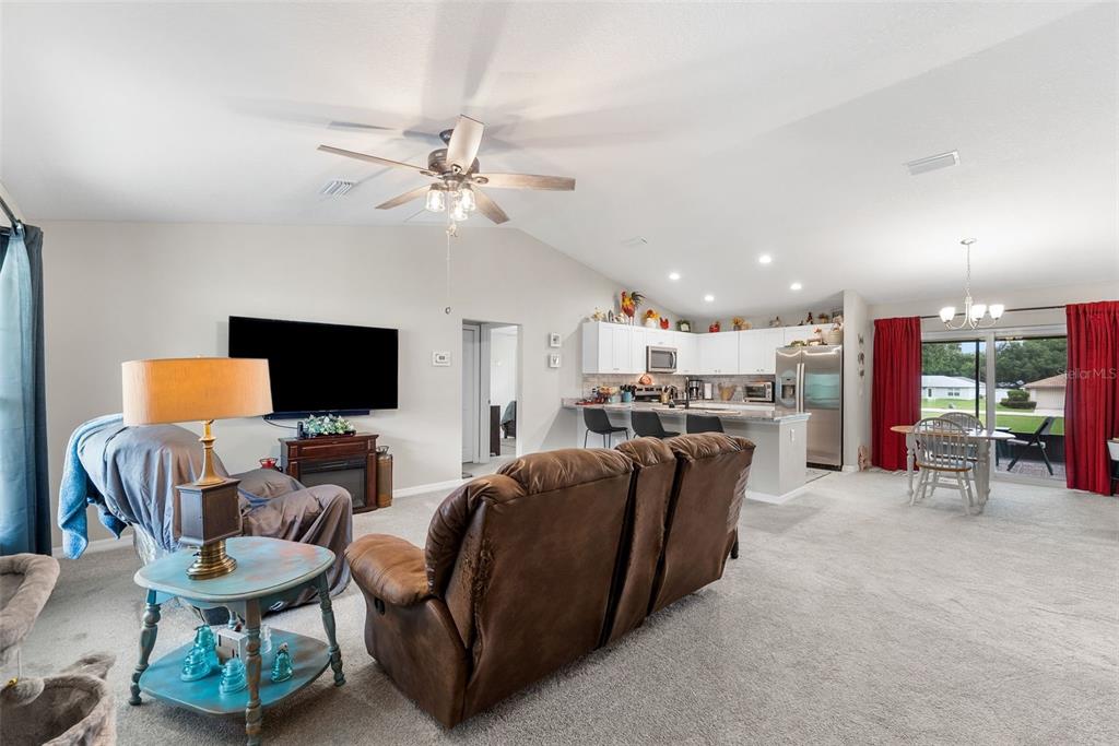 An open-concept living room and kitchen feature carpeted floors, a ceiling fan, and sliding doors — 1831 NE 160TH PLACE, CITRA, FL