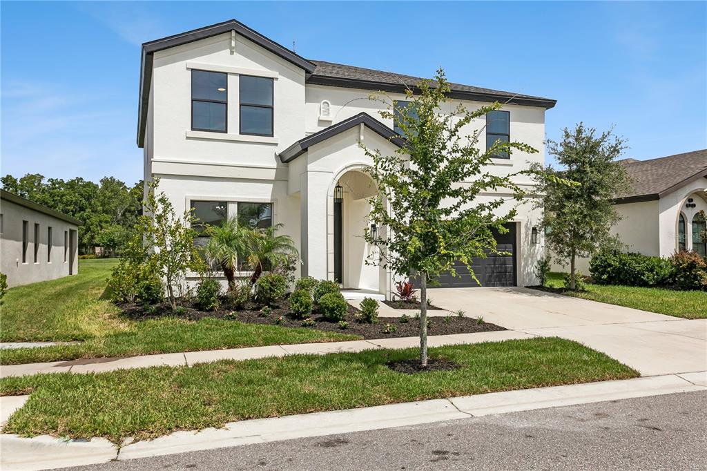 A two-story, white stucco house with a dark roof, arched entryway, and attached garage — 12633 SHETLAND WALK DRIVE, LITHIA, FL