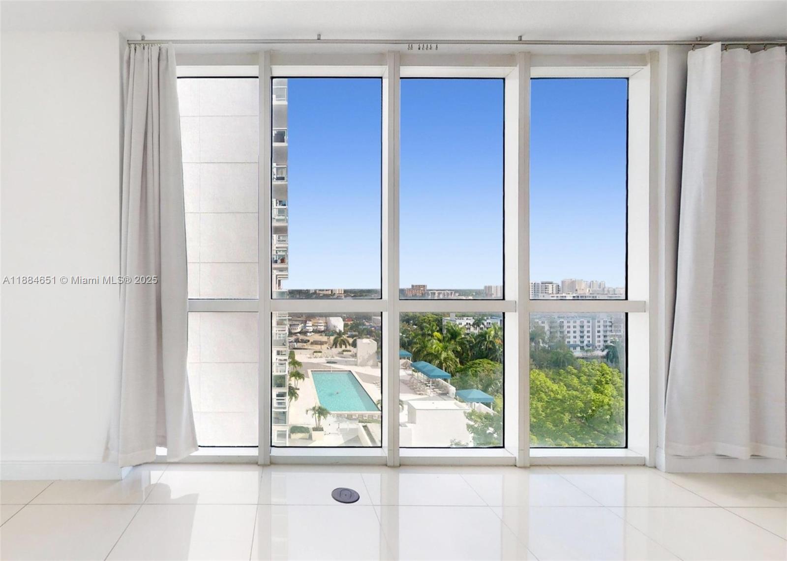 A room with white tiled floors and large windows overlooking a pool and city skyline — 1871 NW S River Dr # 1205, Miami FL 33125, MIAMI, FL