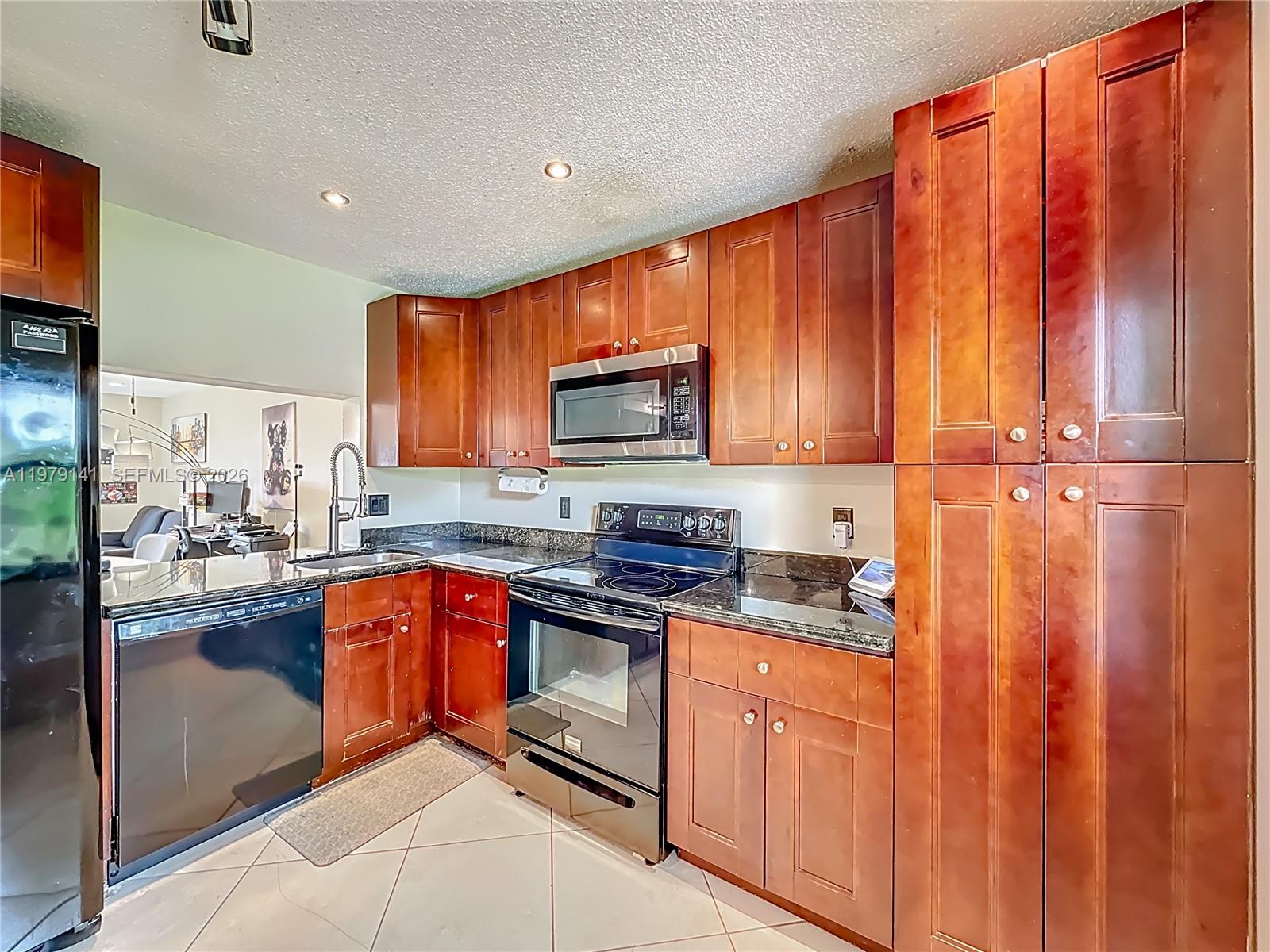A kitchen features cherry wood cabinets, black appliances, and dark granite countertops — 8422 E Boca Glades Blvd E # 8422, Boca Raton FL 33434, BOCA RATON, FL