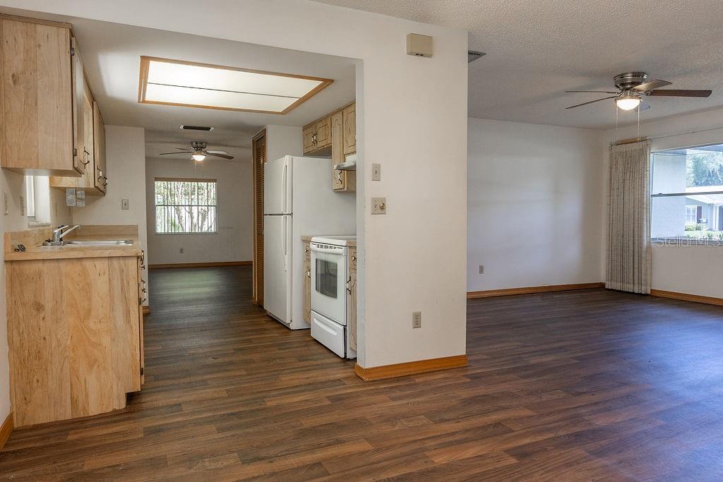 A kitchen with wood cabinets and white appliances opens into a living area with flooring — 919 E MICHIGAN AVENUE, DELAND, FL