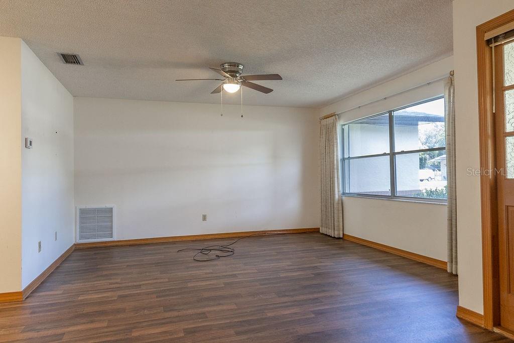 An empty living room features wood-look flooring, a ceiling fan, and a large window — 919 E MICHIGAN AVENUE, DELAND, FL