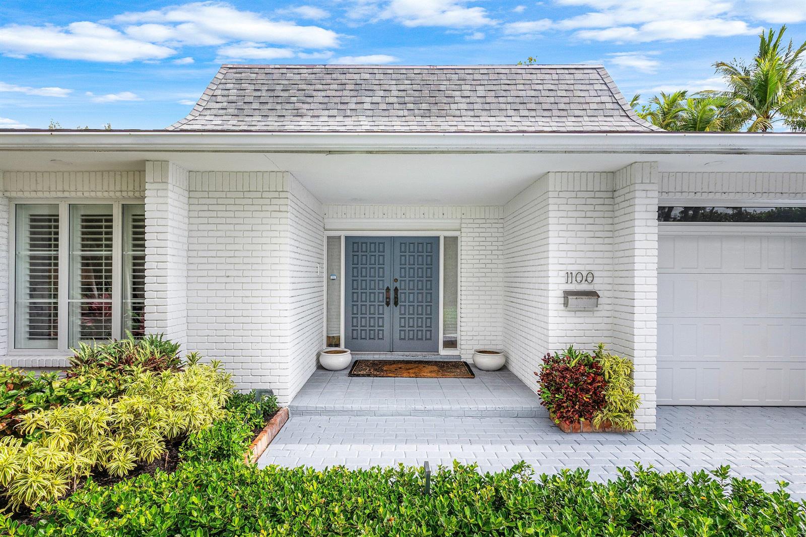 The exterior of a white brick house features a gray double door and a garage — 1100 N Ocean Boulevard, Gulf Stream FL 33483, GULF STREAM, FL