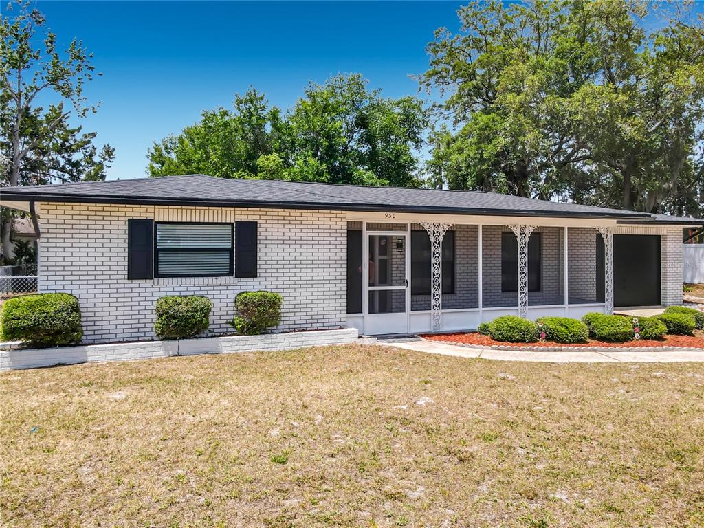 A single-story white brick house features a screened front porch and a black roof — 930 TROY DRIVE, DELTONA, FL