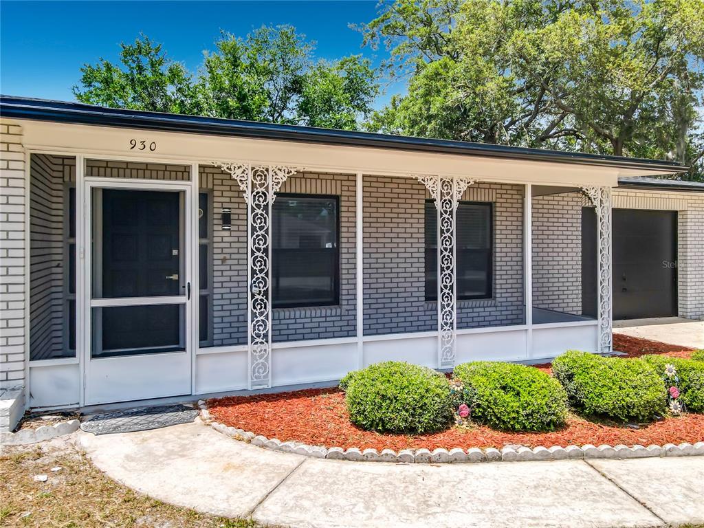 A single-story house exterior features gray brick walls, a screened porch, and white decorative columns — 930 TROY DRIVE, DELTONA, FL