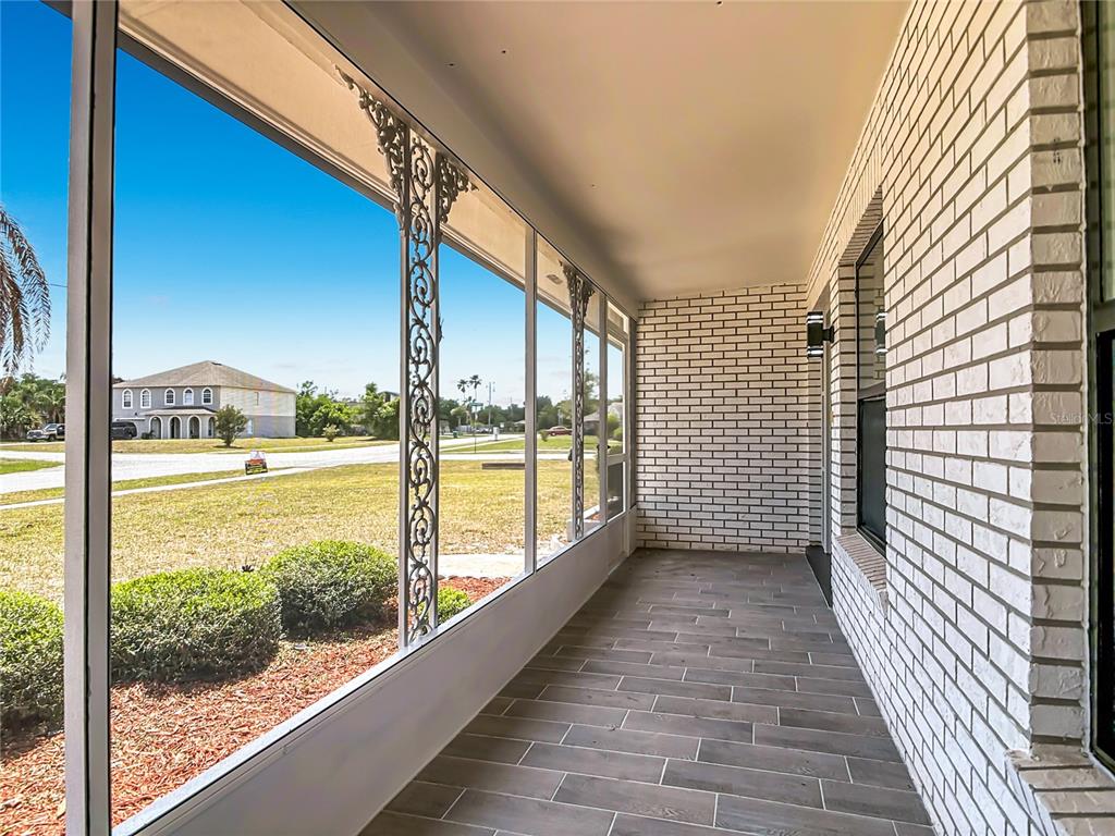 A screened-in porch features white brick walls, gray tile flooring, and decorative metal support columns — 930 TROY DRIVE, DELTONA, FL