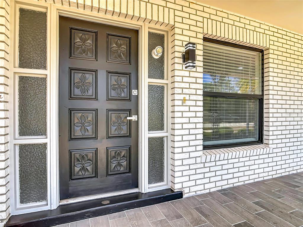 A black front door with floral panels is flanked by glass sidelights on a brick porch — 930 TROY DRIVE, DELTONA, FL