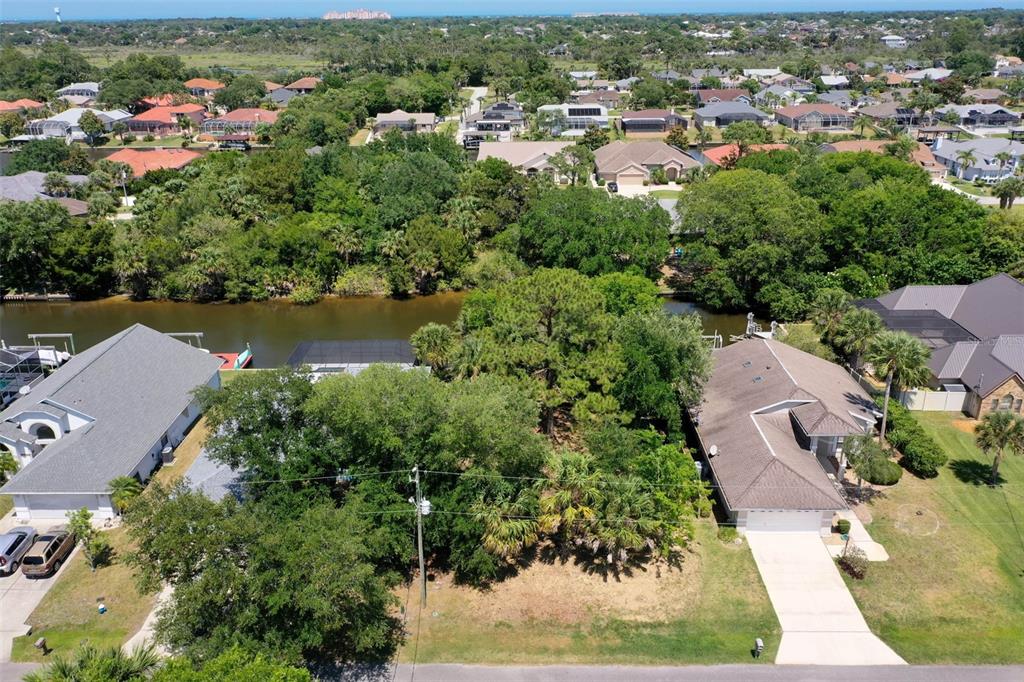 An aerial view shows a residential lot with trees situated between two houses and a canal — 6 CORONA COURT, PALM COAST, FL