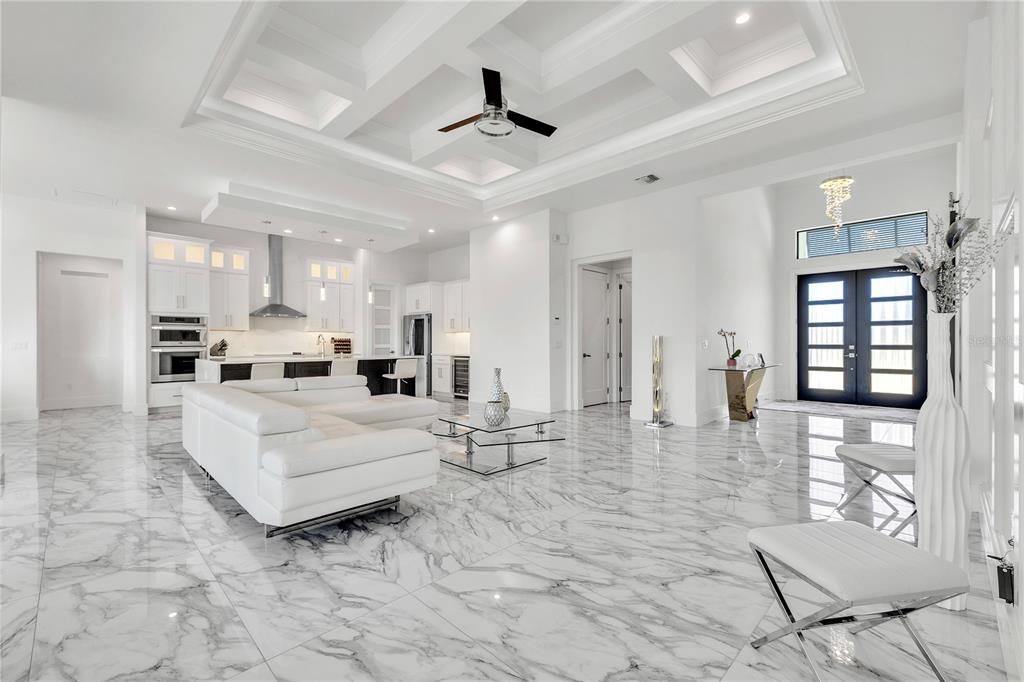 A spacious white open-concept living room and kitchen featuring marble flooring and coffered ceilings — 1323 PENGUIN COURT, PUNTA GORDA, FL