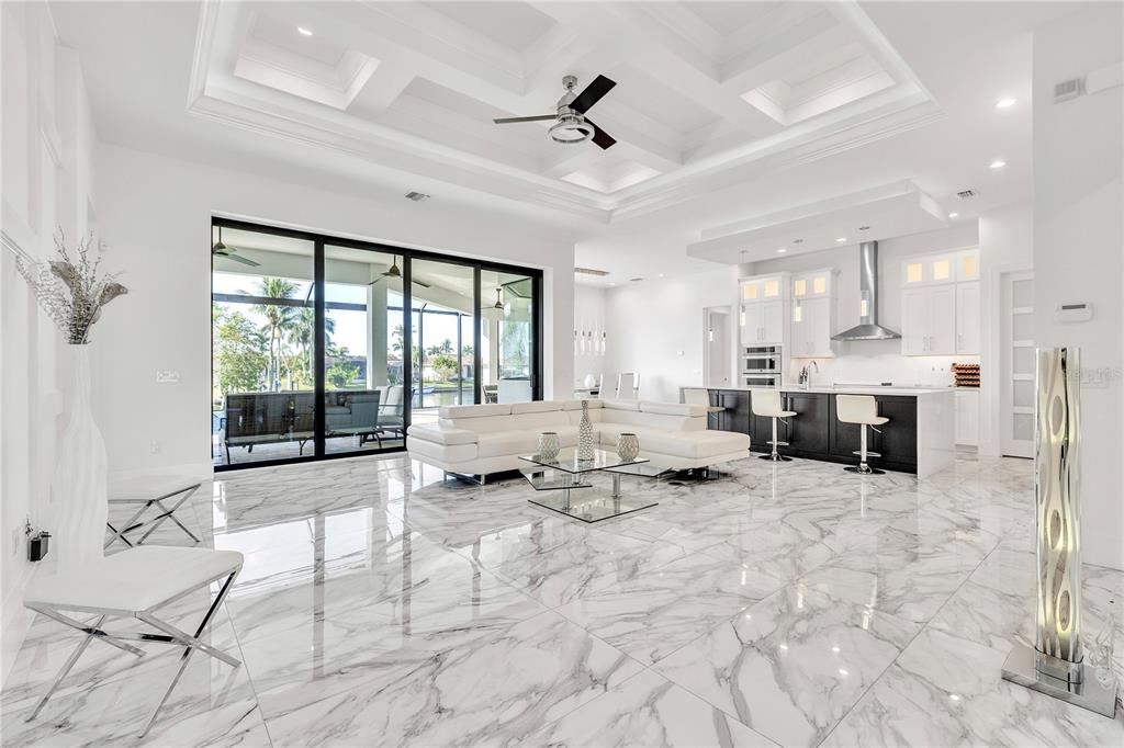A modern open-concept living room and kitchen featuring white marble floors and a coffered ceiling — 1323 PENGUIN COURT, PUNTA GORDA, FL