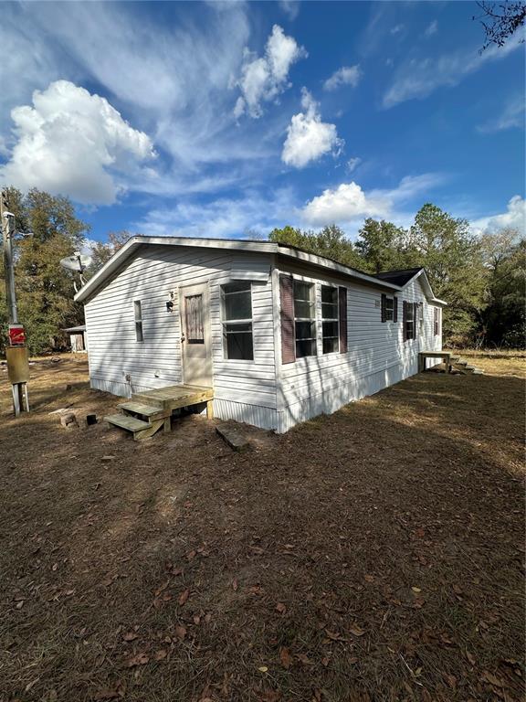 A white mobile home with a wooden porch sits on a dirt lot under trees — 28430 SW 97TH LANE, NEWBERRY, FL