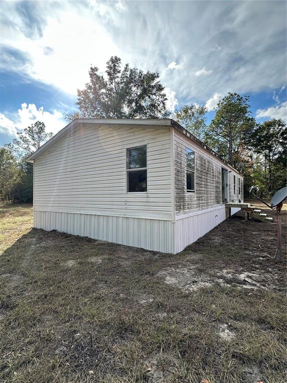 The exterior of a single-wide mobile home with light-colored siding and a satellite dish — 28430 SW 97TH LANE, NEWBERRY, FL