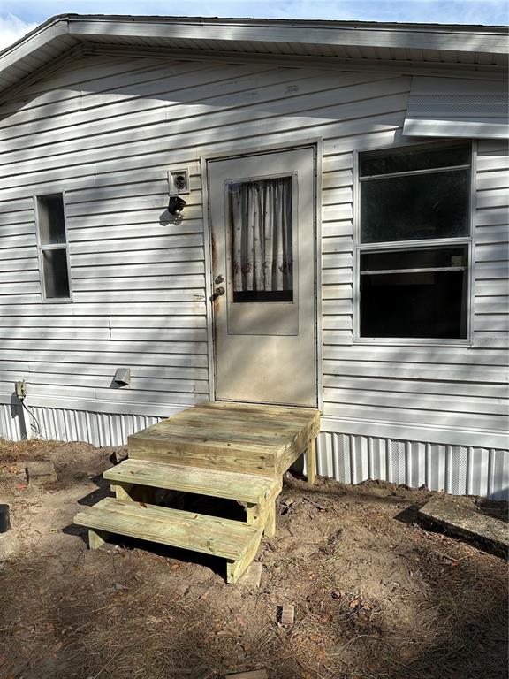The exterior of a mobile home features white vinyl siding, a door, and wooden steps — 28430 SW 97TH LANE, NEWBERRY, FL