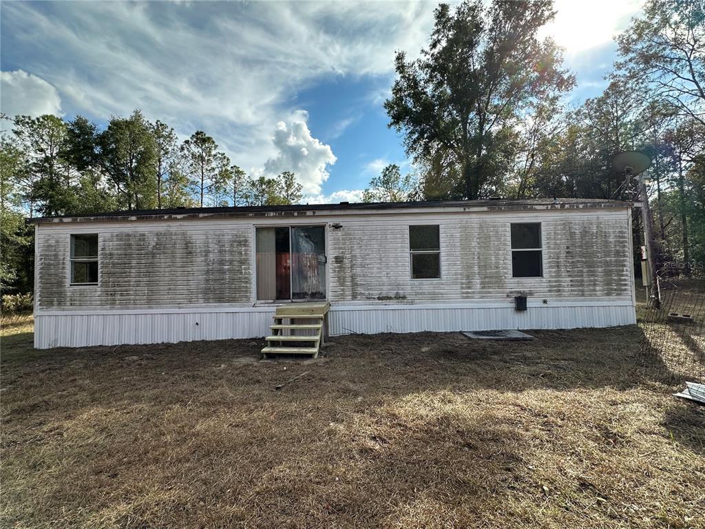 The exterior of a weathered, single-wide mobile home features white siding and a small wooden staircase — 28430 SW 97TH LANE, NEWBERRY, FL