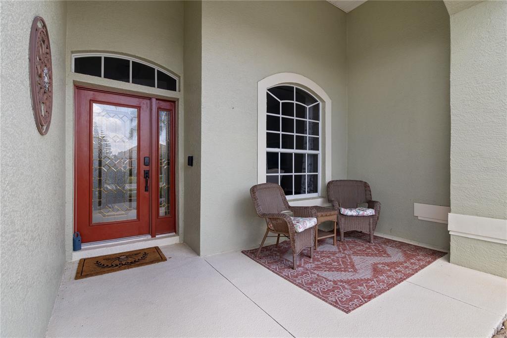 A covered front porch features a red door, a window, and two wicker chairs on a rug — 2725 ROYAL PALM DRIVE, NORTH PORT, FL
