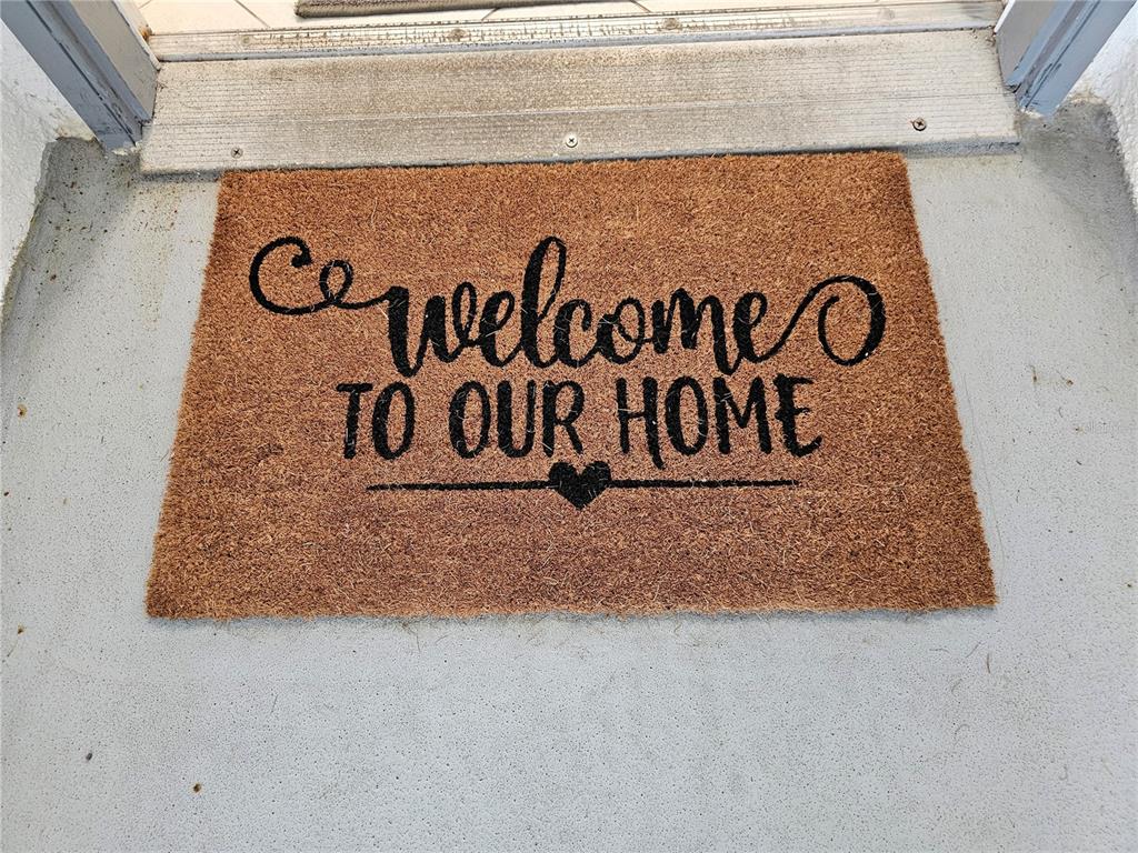 A brown coir doormat with the text "welcome TO OUR HOME" sits on a concrete porch — 5207 S ATLANTIC AVENUE UNIT 722, NEW SMYRNA BEACH, FL