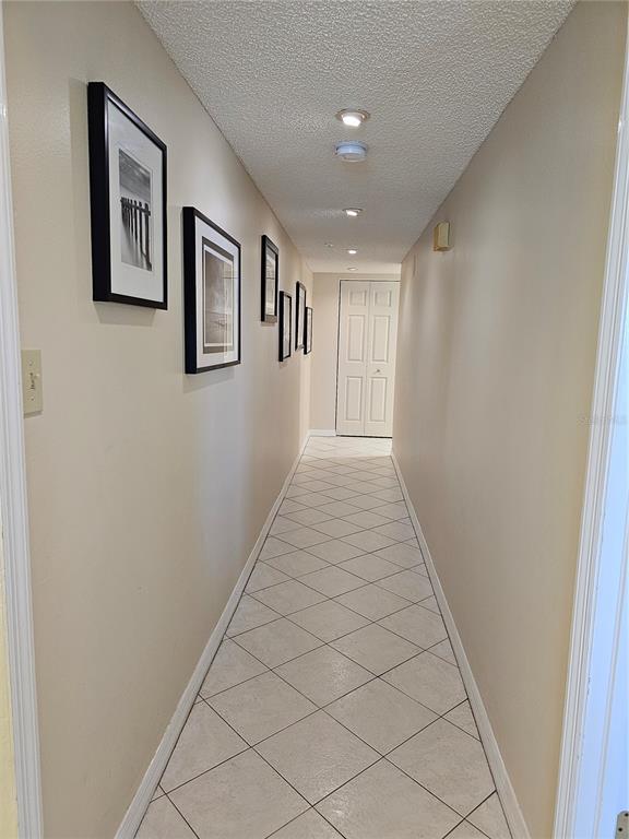 A narrow hallway features beige walls, framed black-and-white photos, and light-colored diagonal floor tiles — 5207 S ATLANTIC AVENUE UNIT 722, NEW SMYRNA BEACH, FL