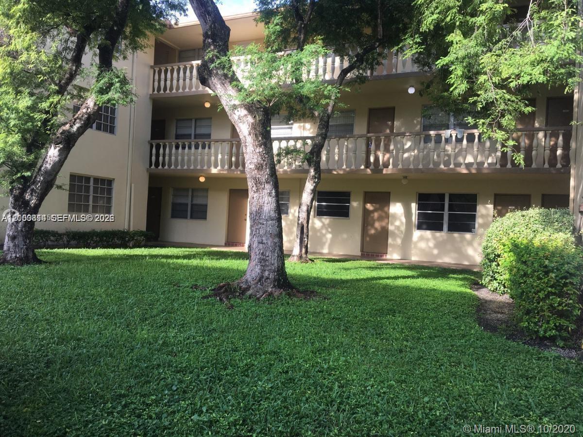 A three-story apartment building with exterior walkways and balconies surrounded by trees and grass — HOLLYWOOD, FL