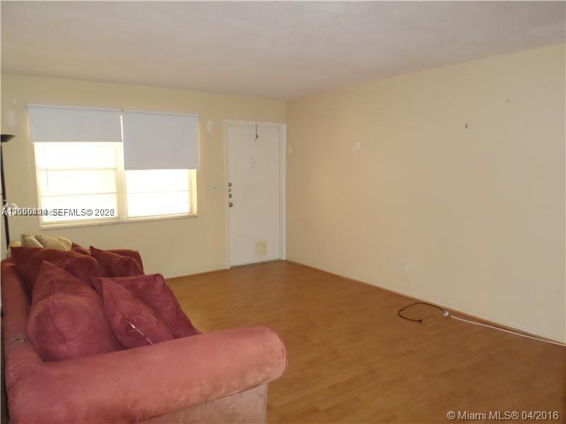 A living room features light-colored walls, wood-look flooring, a white door, and a red sofa — HOLLYWOOD, FL