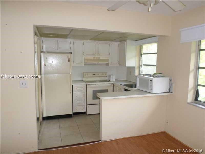 A kitchen with white cabinets, a white refrigerator, and a white stove, viewed from an adjacent room — HOLLYWOOD, FL