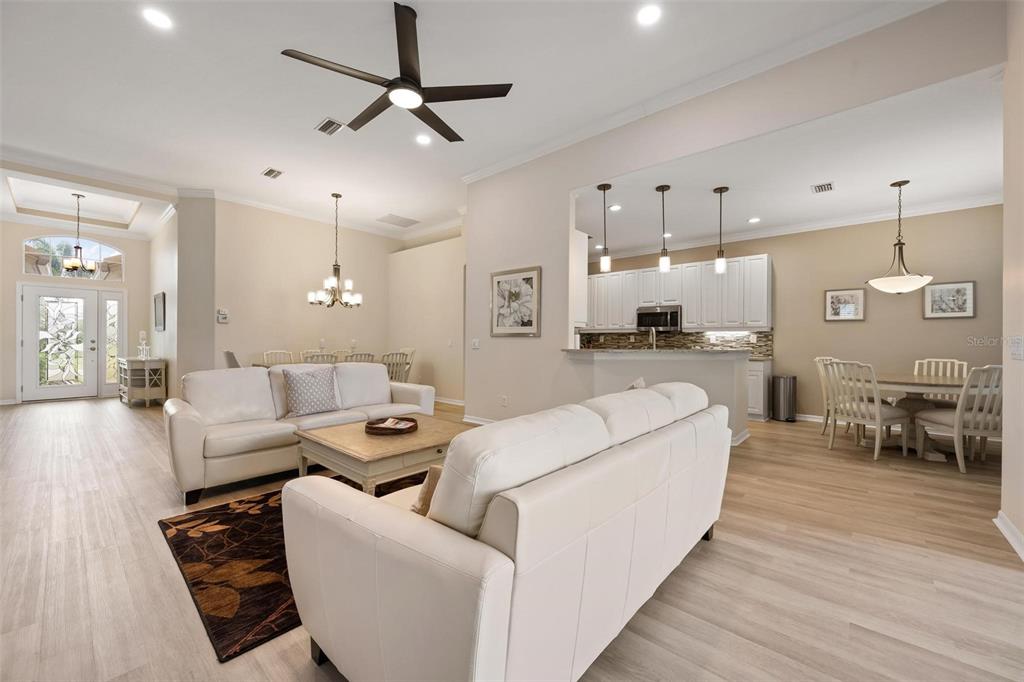 A living room with white sofas and a ceiling fan opens into a kitchen and dining area — 748 BACK NINE DRIVE, VENICE, FL