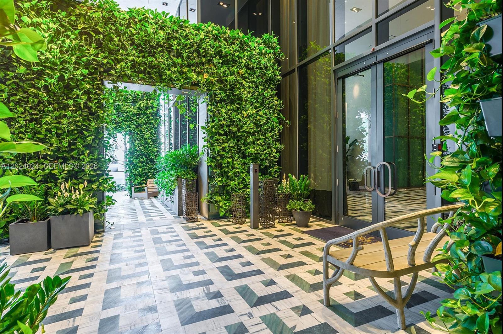 A modern building entrance features a patterned tile floor, glass doors, and lush vertical greenery — 801 S Miami Ave # 4405, Miami FL 33130, MIAMI, FL