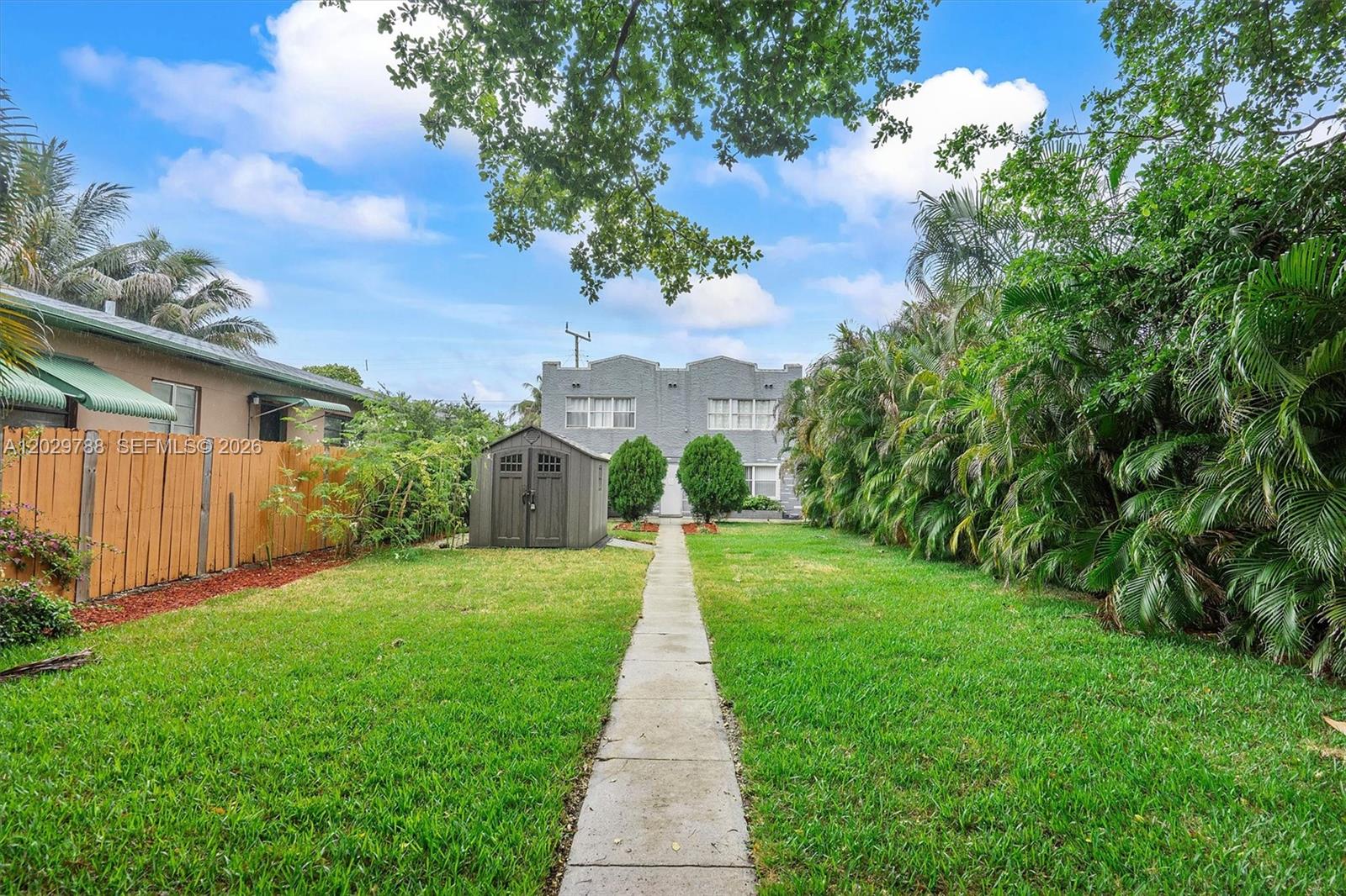 A backyard features a concrete path leading to a gray shed and a two-story building — 1940 Adams St, Hollywood FL 33020, HOLLYWOOD, FL