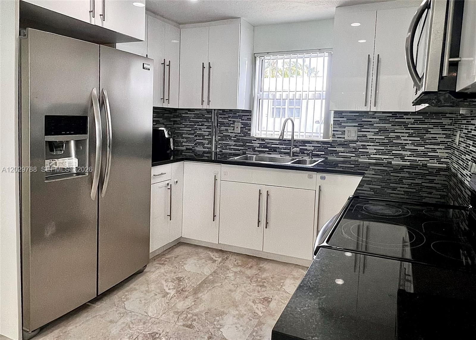A kitchen features white cabinets, stainless steel appliances, black countertops, and a tiled backsplash — 1940 Adams St, Hollywood FL 33020, HOLLYWOOD, FL