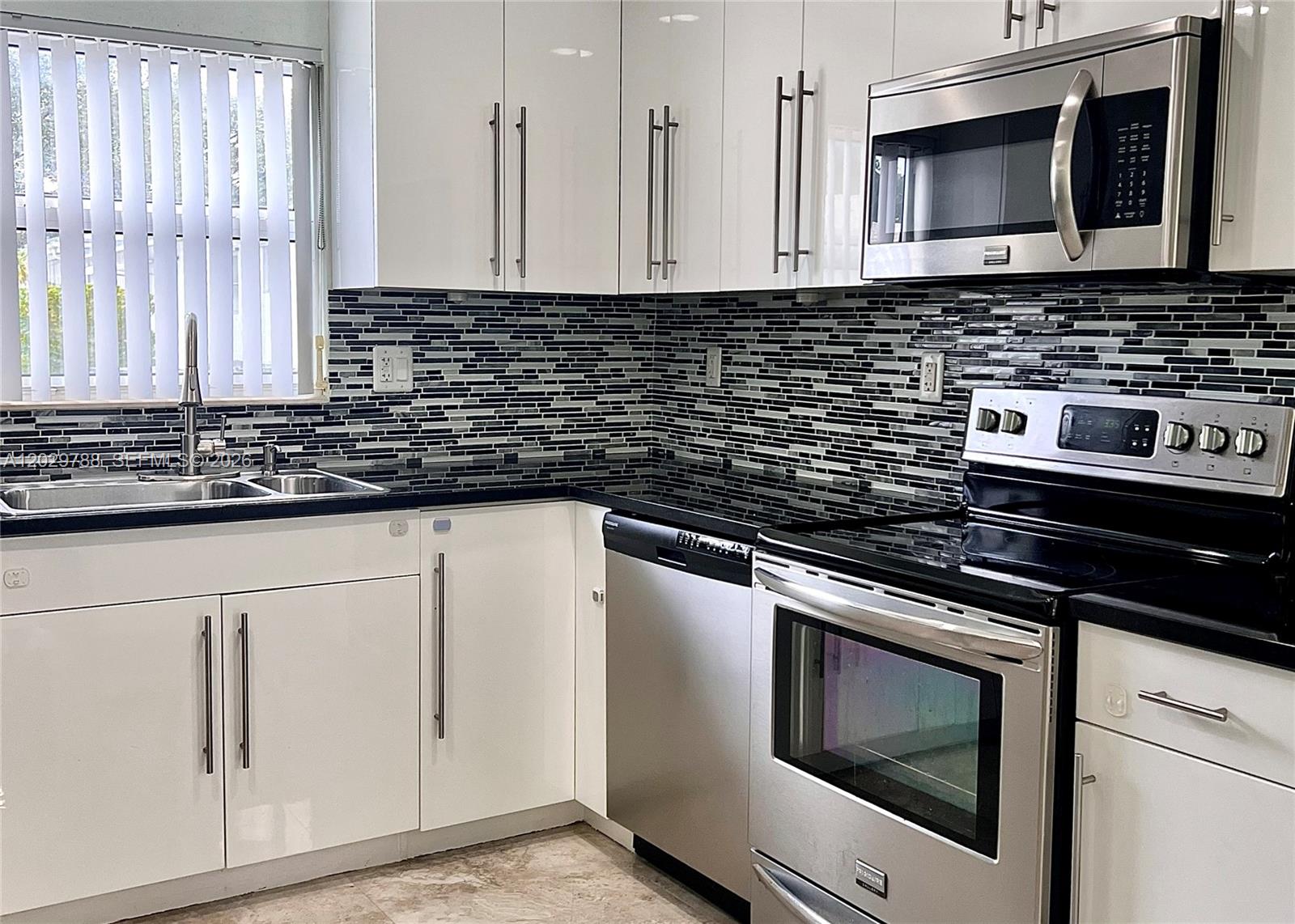 A kitchen features white cabinets, stainless steel appliances, black countertops, and a mosaic tile backsplash — 1940 Adams St, Hollywood FL 33020, HOLLYWOOD, FL