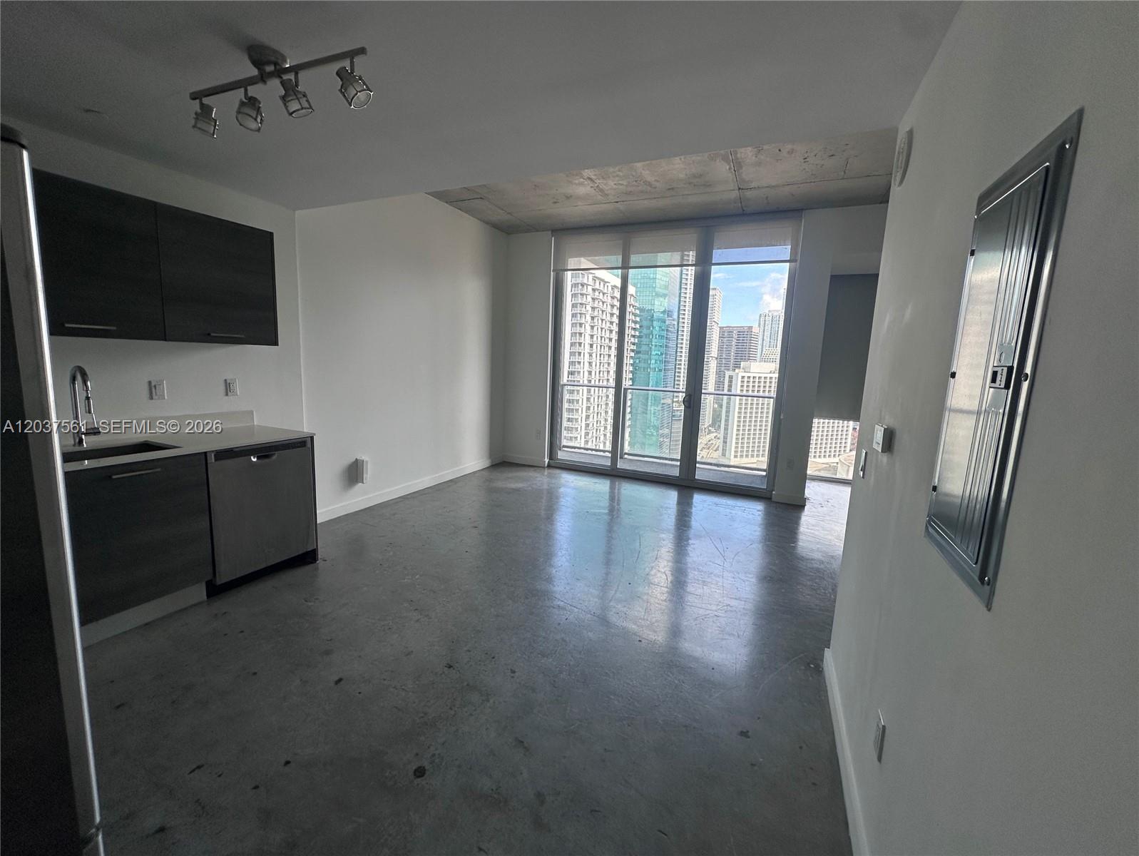 A studio apartment features a kitchenette, concrete floors, exposed ceiling, and floor-to-ceiling windows — 151 SE 1st St # 2405, Miami FL 33131, MIAMI, FL