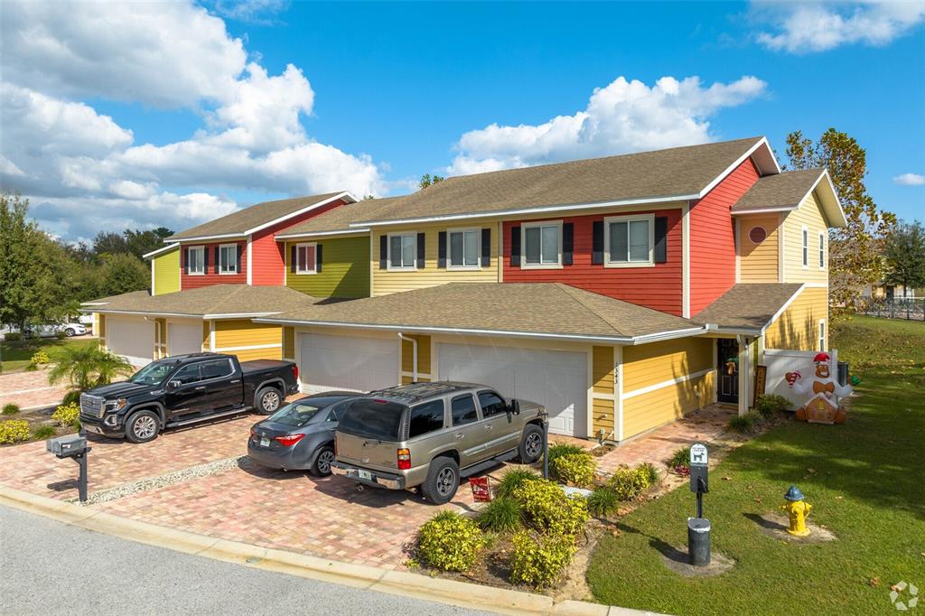 A multi-unit townhouse exterior with colorful siding, a paver driveway, and three parked vehicles — 1125 EVERGREEN COURT, WINTER HAVEN, FL