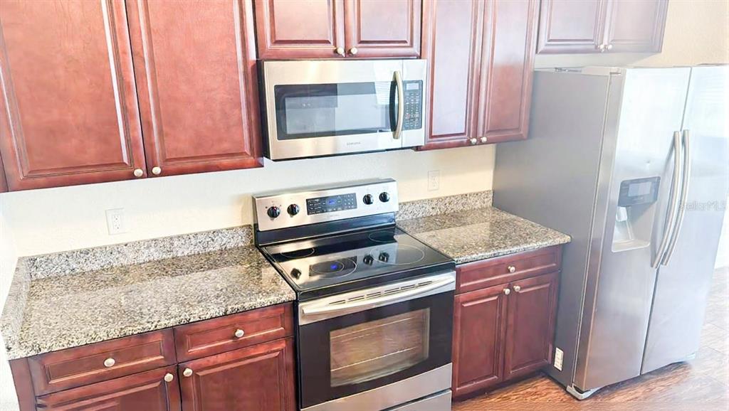 A kitchen features dark wood cabinets, granite countertops, and stainless steel appliances — 1125 EVERGREEN COURT, WINTER HAVEN, FL