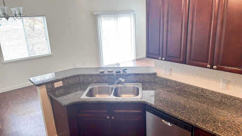 A kitchen features dark wood cabinets, granite countertops, a double sink, and stainless steel appliances — 1125 EVERGREEN COURT, WINTER HAVEN, FL