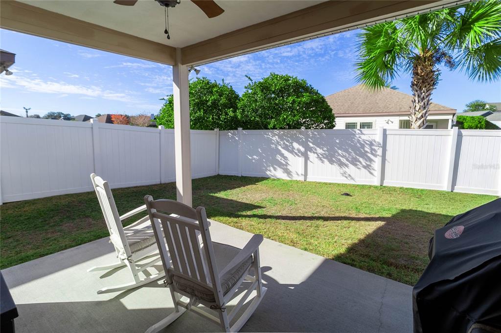 A covered concrete patio with two rocking chairs overlooks a fenced backyard with a palm tree — 1852 SW 246TH DRIVE, NEWBERRY, FL