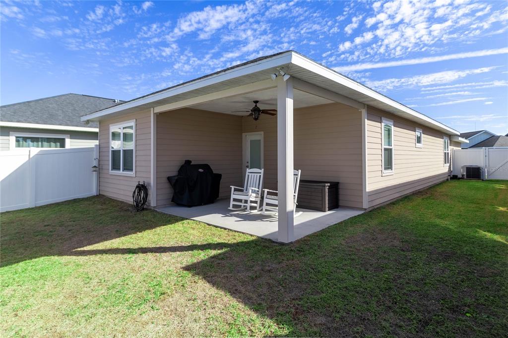 A covered concrete patio features two white rocking chairs, a grill, and a storage chest — 1852 SW 246TH DRIVE, NEWBERRY, FL
