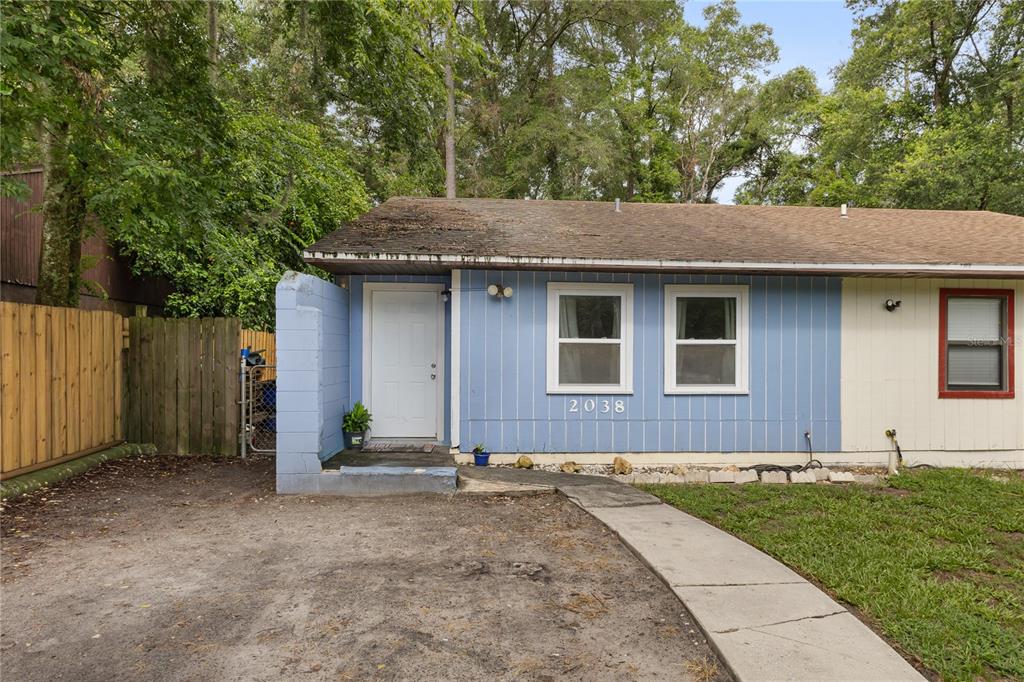 A single-story house with blue vertical siding, a white front door, and a concrete walkway — 2038 SW 70TH TERRACE, GAINESVILLE, FL
