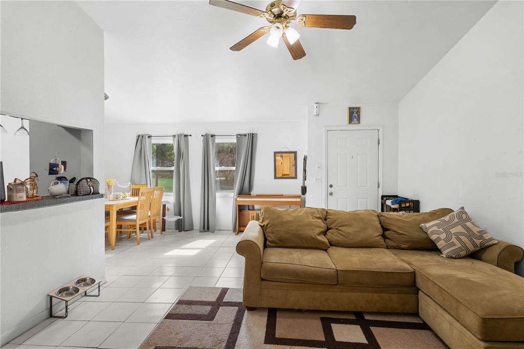 A living room with a tan sectional sofa, tile flooring, and an adjacent dining area — 2038 SW 70TH TERRACE, GAINESVILLE, FL
