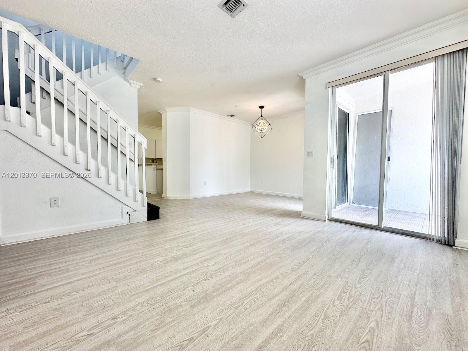 An empty living room features light wood-look flooring, a white staircase, and sliding glass doors — 4371 SW 160th Ave # 203, Miramar FL 33027, MIRAMAR, FL