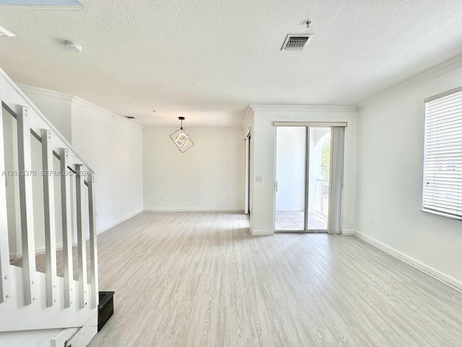 An empty room features light wood-look flooring, white walls, a staircase, and a sliding glass door — 4371 SW 160th Ave # 203, Miramar FL 33027, MIRAMAR, FL