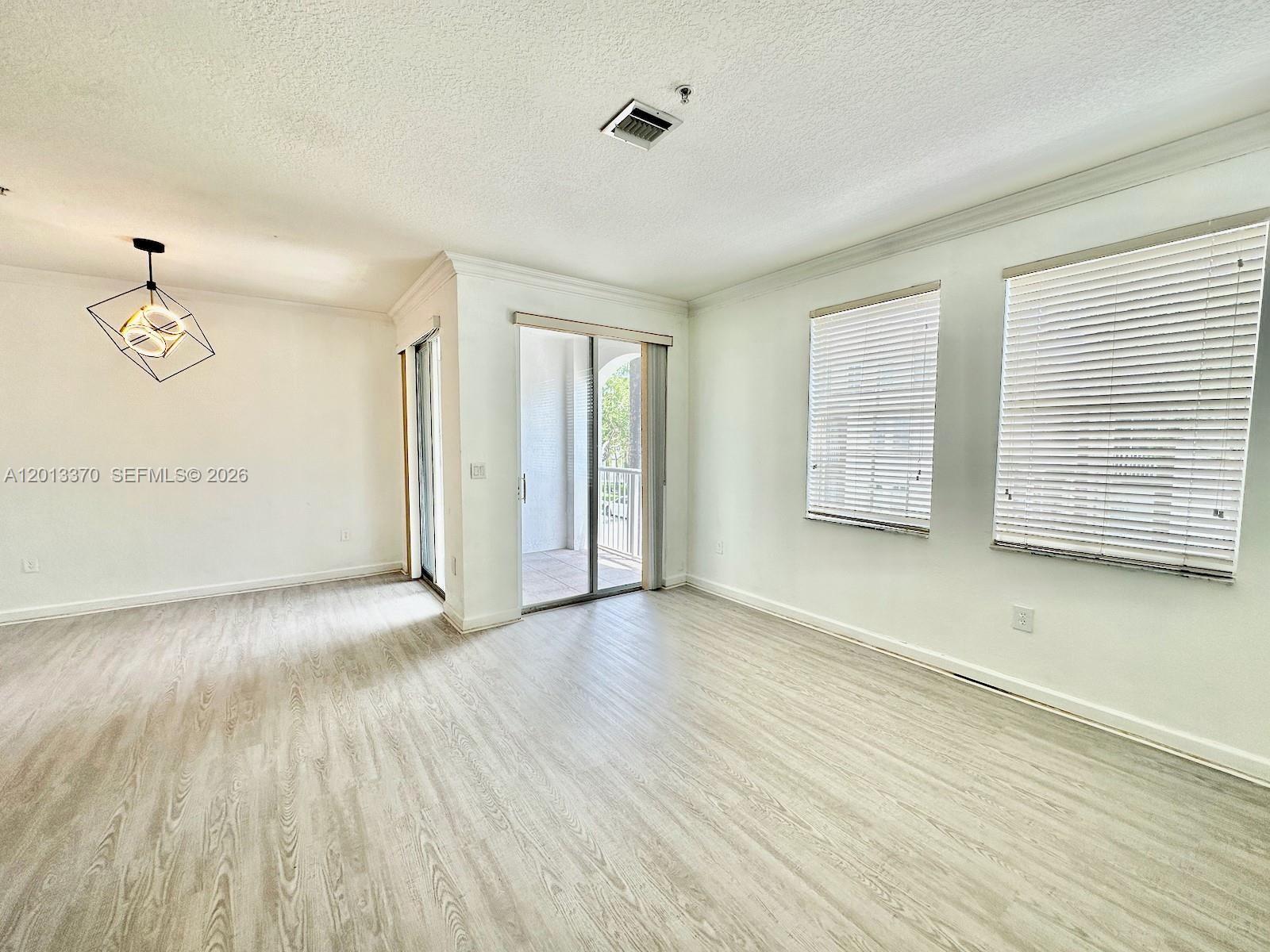 An empty room features light wood-look flooring, white walls, a modern light fixture, and balcony access — 4371 SW 160th Ave # 203, Miramar FL 33027, MIRAMAR, FL