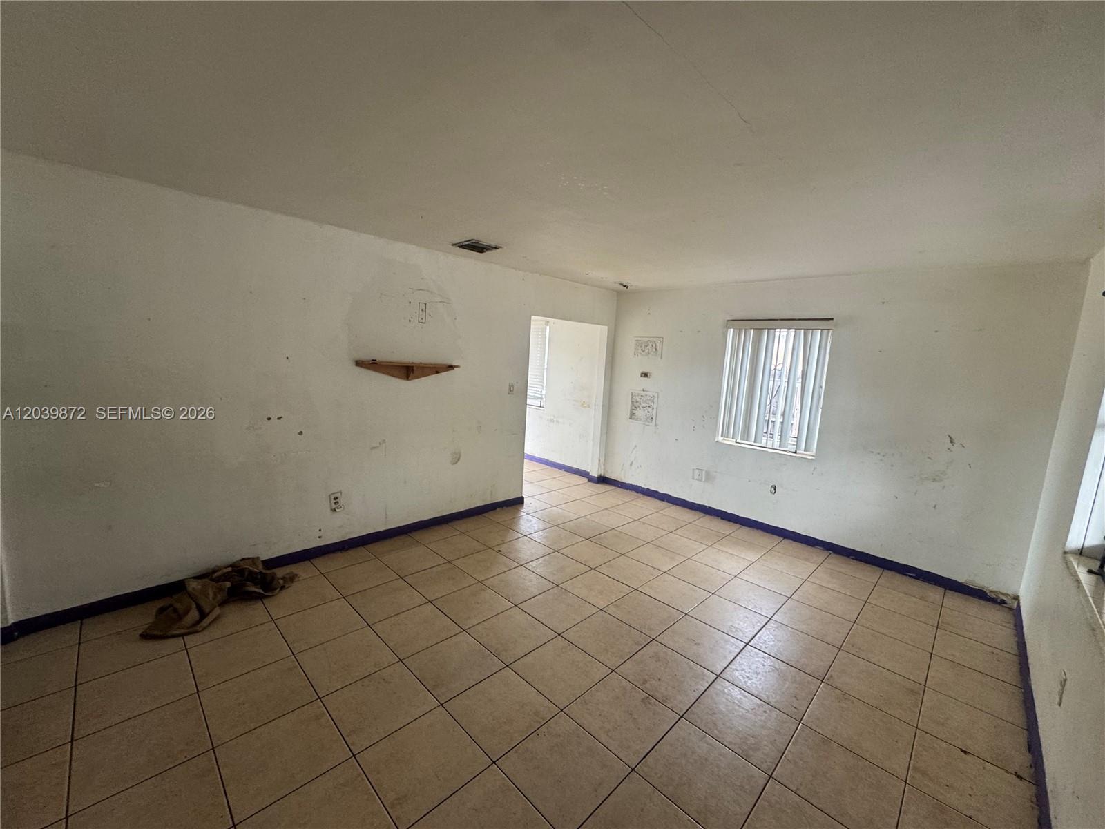 An empty room features white walls, tan tile flooring, and a single window with blinds — 3320 NW 87th Ter, Miami FL 33147, MIAMI, FL