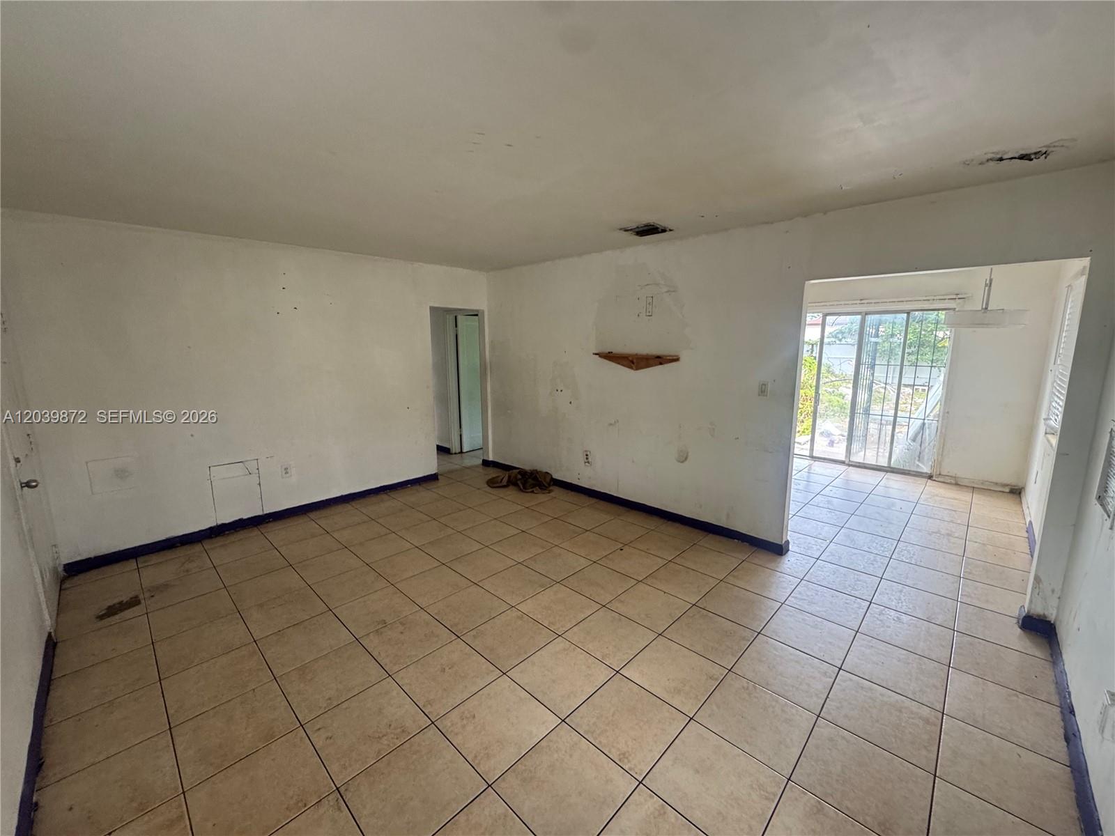 An empty room with beige tile flooring, white walls, and a sliding glass door — 3320 NW 87th Ter, Miami FL 33147, MIAMI, FL