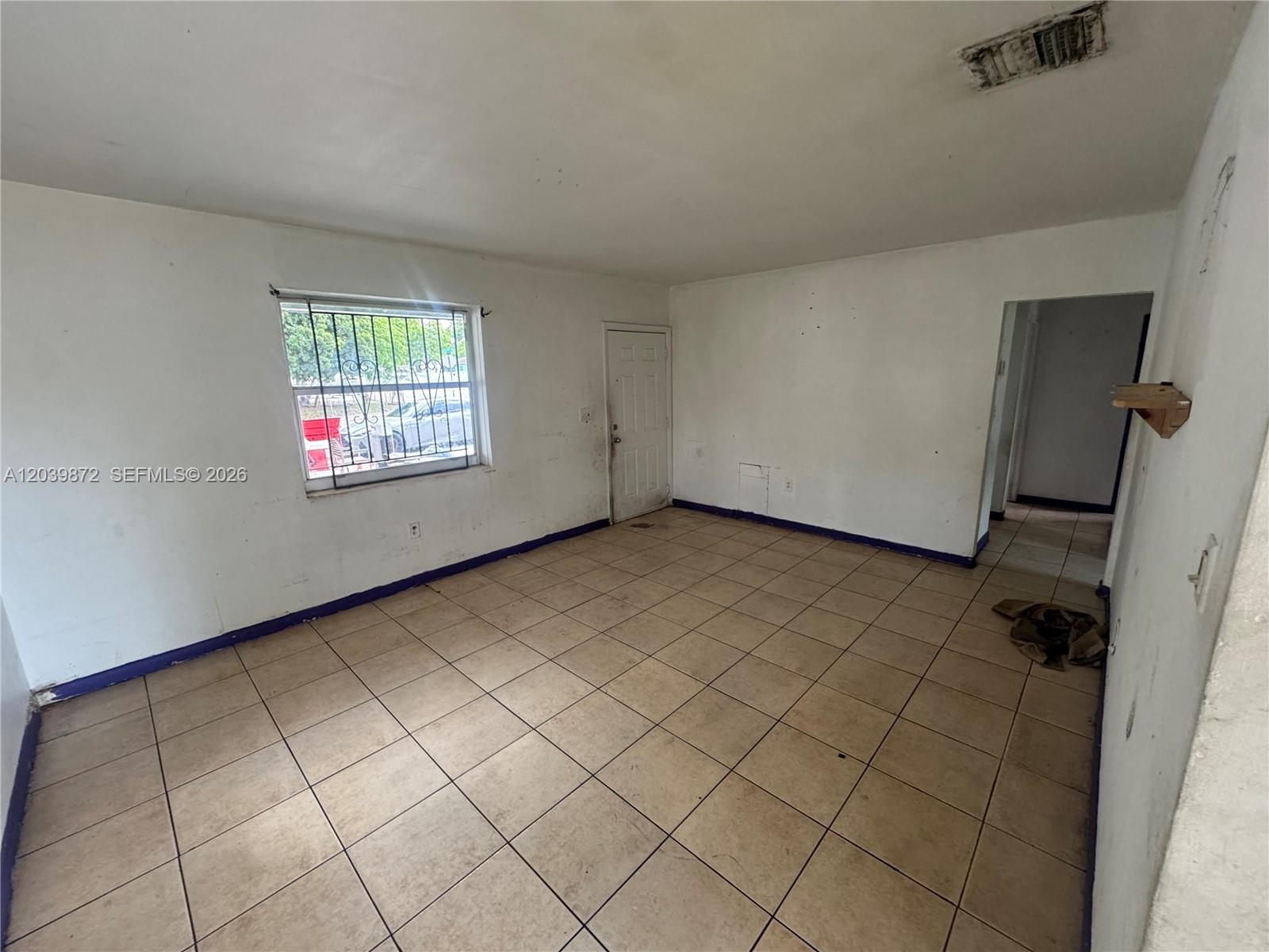 An empty room features white walls, tiled floors, a window with security bars, and a doorway — 3320 NW 87th Ter, Miami FL 33147, MIAMI, FL