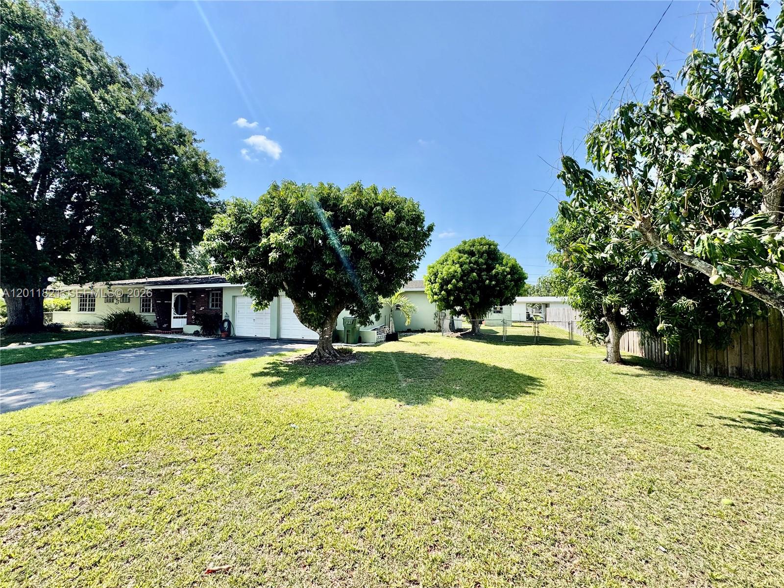 A single-story house with a two-car garage sits on a grassy lot with trees — 434 NW 20th St, Homestead FL 33030, HOMESTEAD, FL