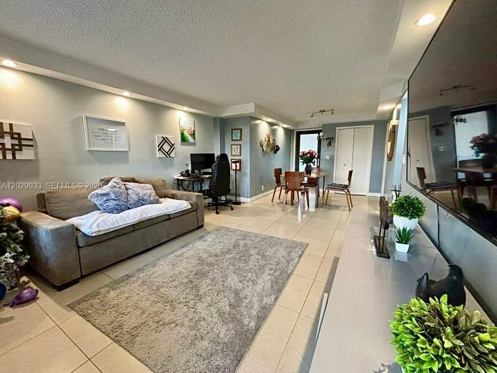 A living room features a grey sofa, a dining area, and tile flooring — 301 Golden Isles Dr # 406, Hallandale Beach FL 33009, HALLANDALE BEACH, FL