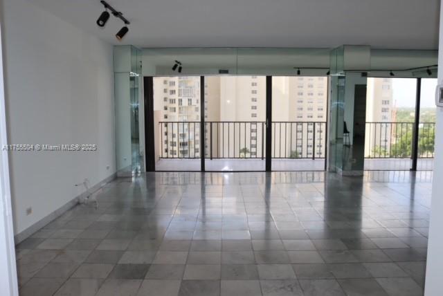 An empty room with light-colored tile flooring, mirrored columns, and a balcony overlooking tall buildings — 1800 NE 114th St # 1108, Miami FL 33181, MIAMI, FL
