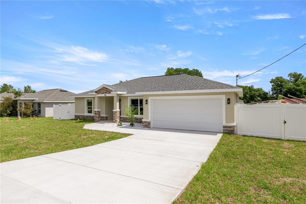 A single-story house with a white garage door, stone accents, and a concrete driveway — 85 JUNIPER LOOP CIRCLE, OCALA, FL