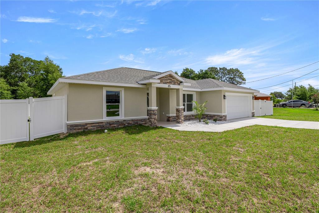 A single-story house with a beige stucco exterior, stone accents, and a white vinyl fence — 85 JUNIPER LOOP CIRCLE, OCALA, FL