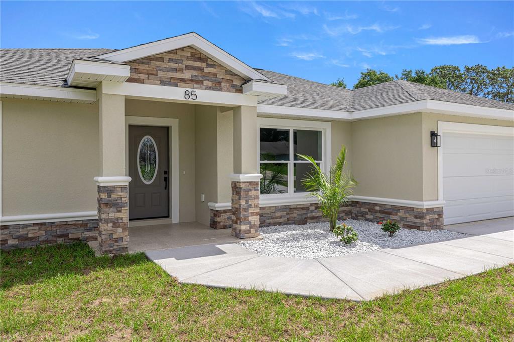 The exterior of a single-story house features a stone-accented porch and a white garage door — 85 JUNIPER LOOP CIRCLE, OCALA, FL